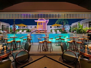 Un espace bar aménagé au bord de la piscine, avec plusieurs tables et chaises, une piscine et un anneau de sauvetage.