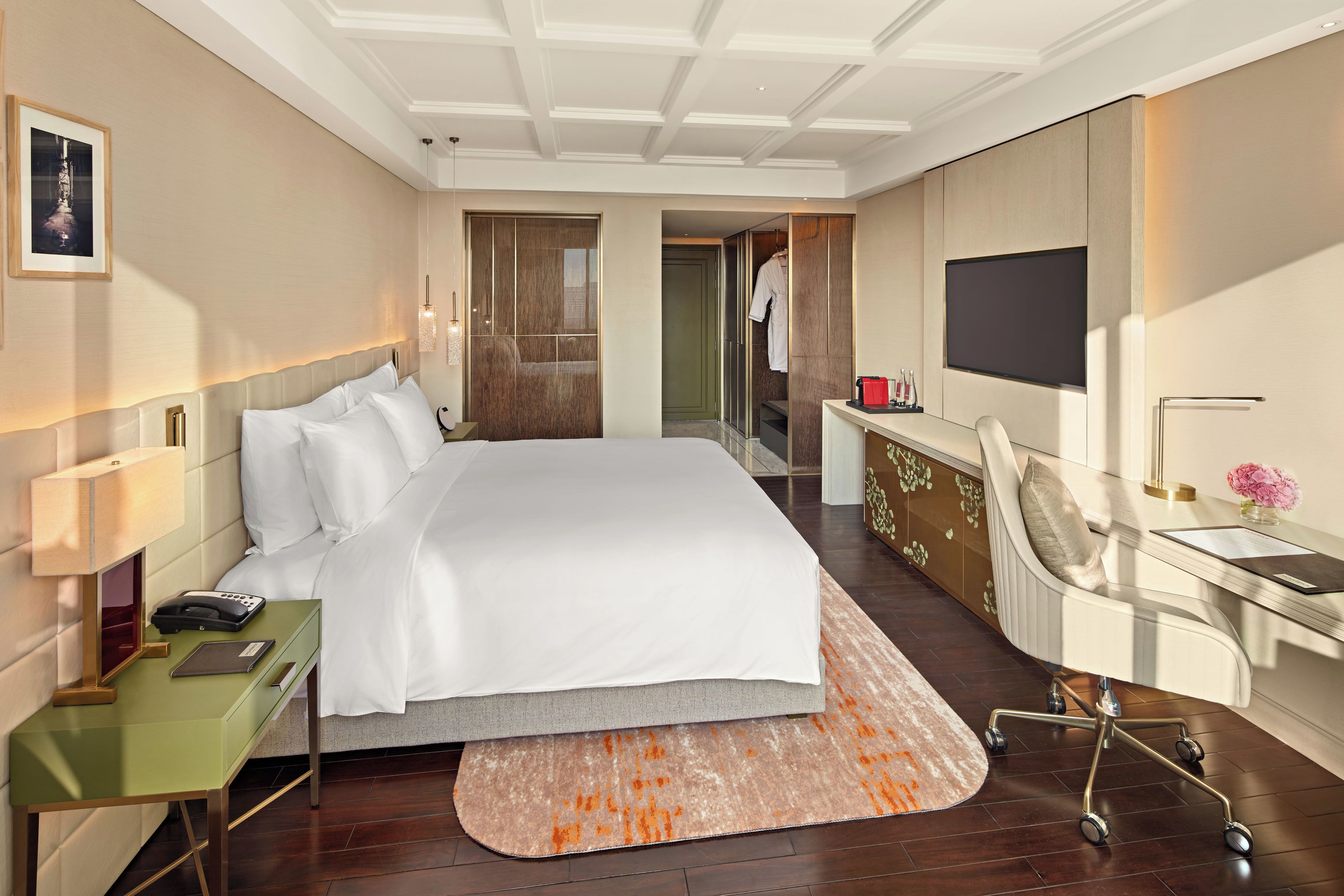 A hotel room with a large bed, bedside table, desk, chair, and a TV mounted on the wall.