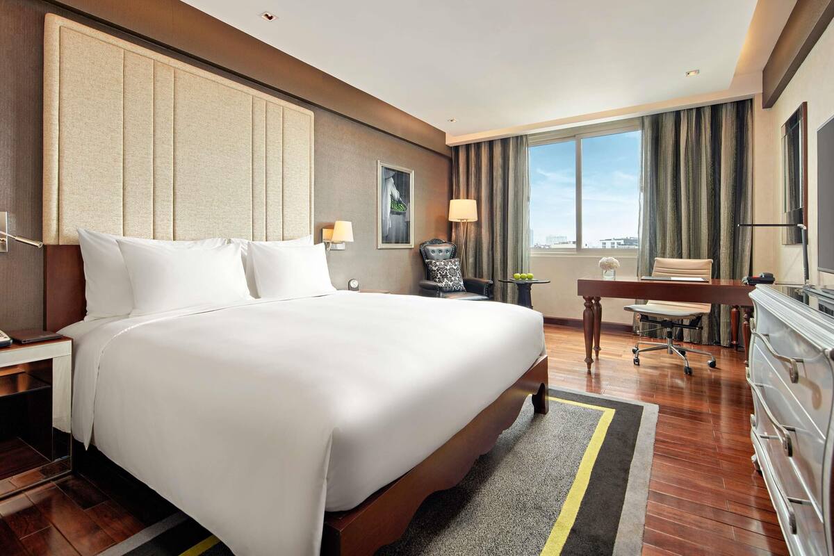 Ein Hotelzimmer mit einem großen Bett, einem Schreibtisch, einem Sessel und Blick auf die Stadt.