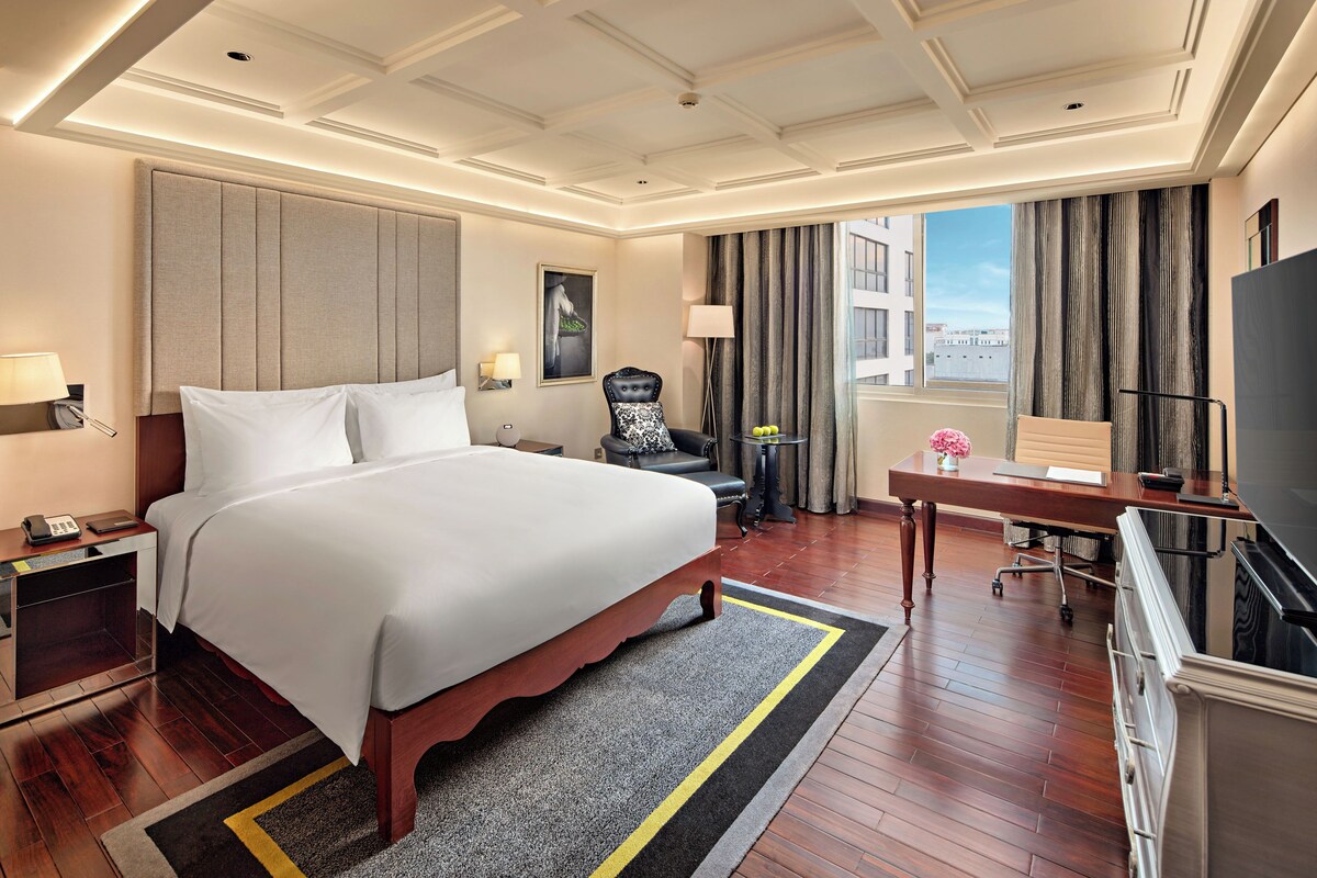 Een hotelkamer met een groot bed, een bureau, een stoel, een televisie en uitzicht over de stad.