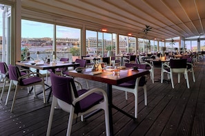 An outdoor restaurant with tables and chairs, large windows, and a view of the cityscape. - InterContinental Malta by IHG (St. Julian's)