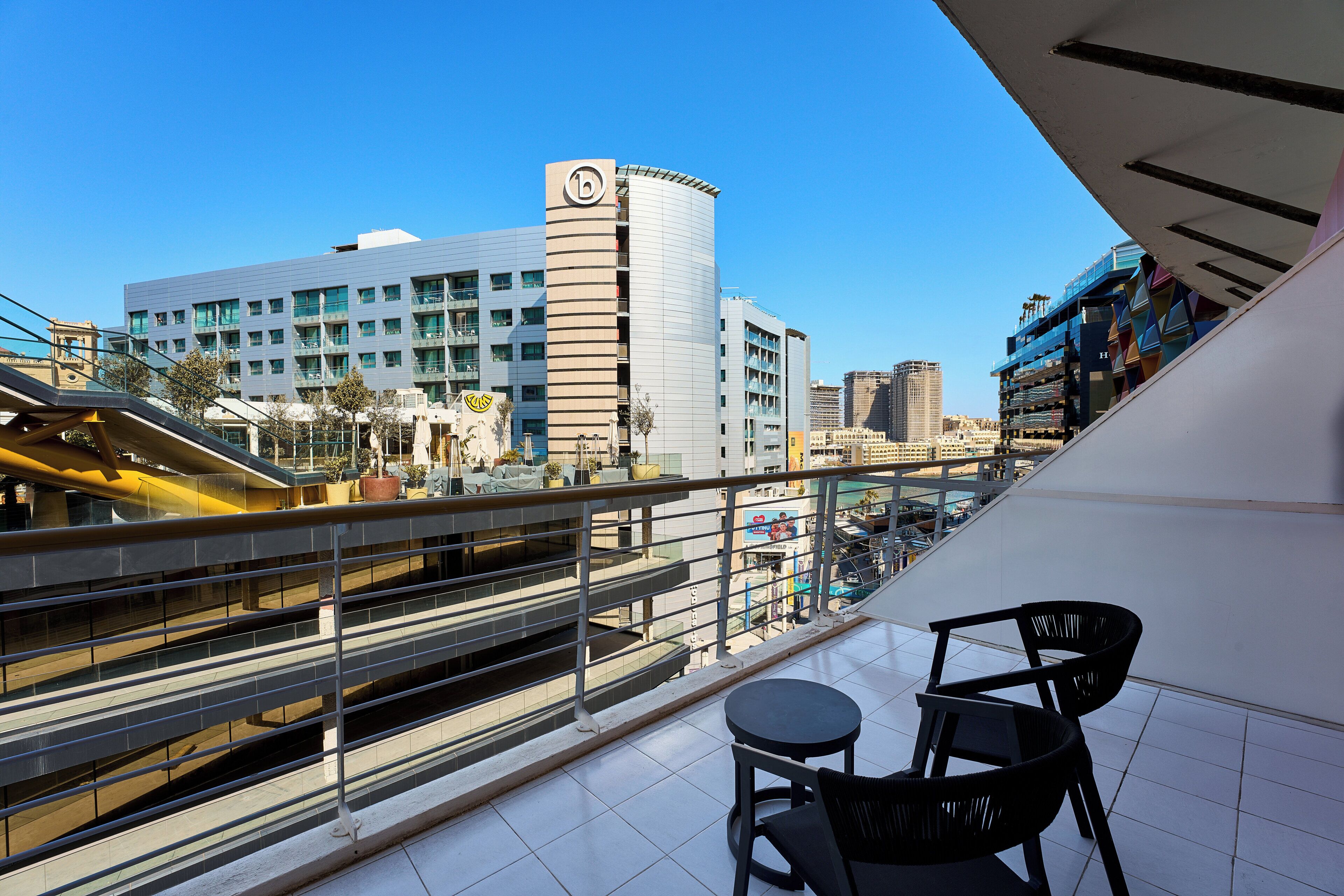 Ein Balkon mit Blick auf ein modernes Gebäude, eine Fußgängerbrücke und einen Parkplatz.