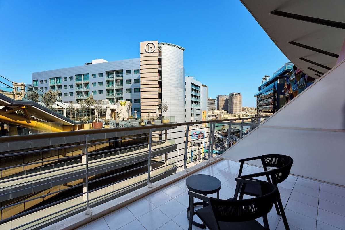 A balcony with a view of a modern building, a pedestrian bridge, and a parking area.