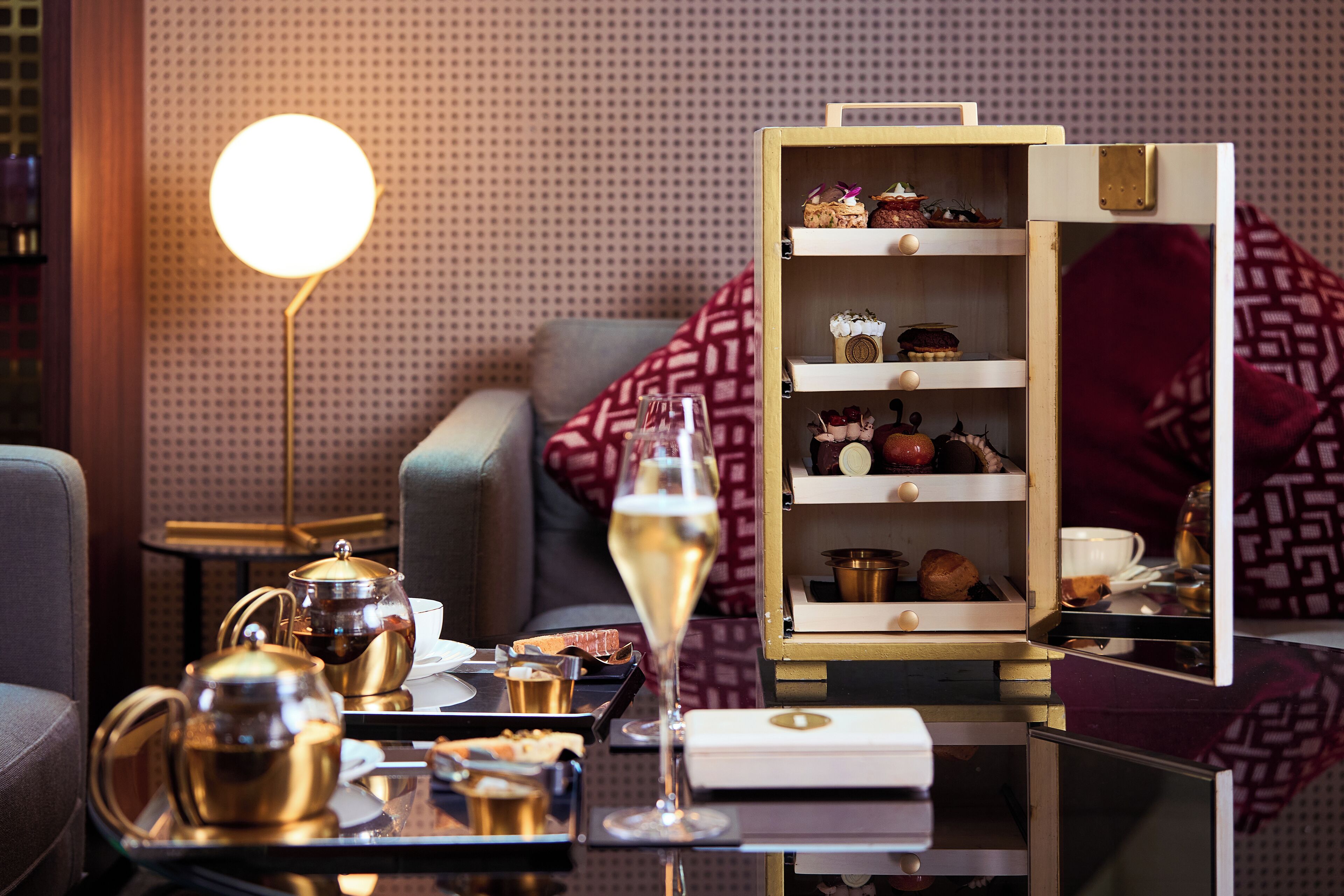 A cozy living area with a coffee table set for tea service, a wine glass, and a decorative wooden cabinet with shelves.