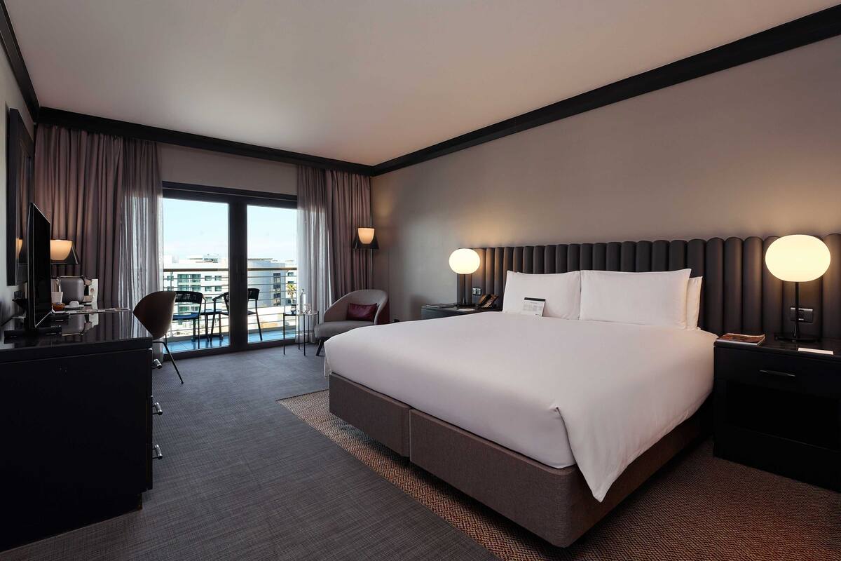 A modern hotel room with a large bed, a desk, and a view of the city.