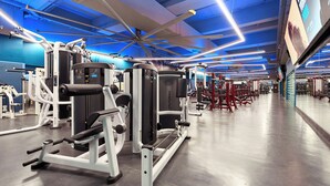 Un gimnasio moderno con diversas máquinas de ejercicio, un espejo grande y un techo iluminado en azul.