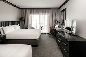 Habitación de hotel con una cama grande, un escritorio con televisor, una silla y una mesita con un florero.