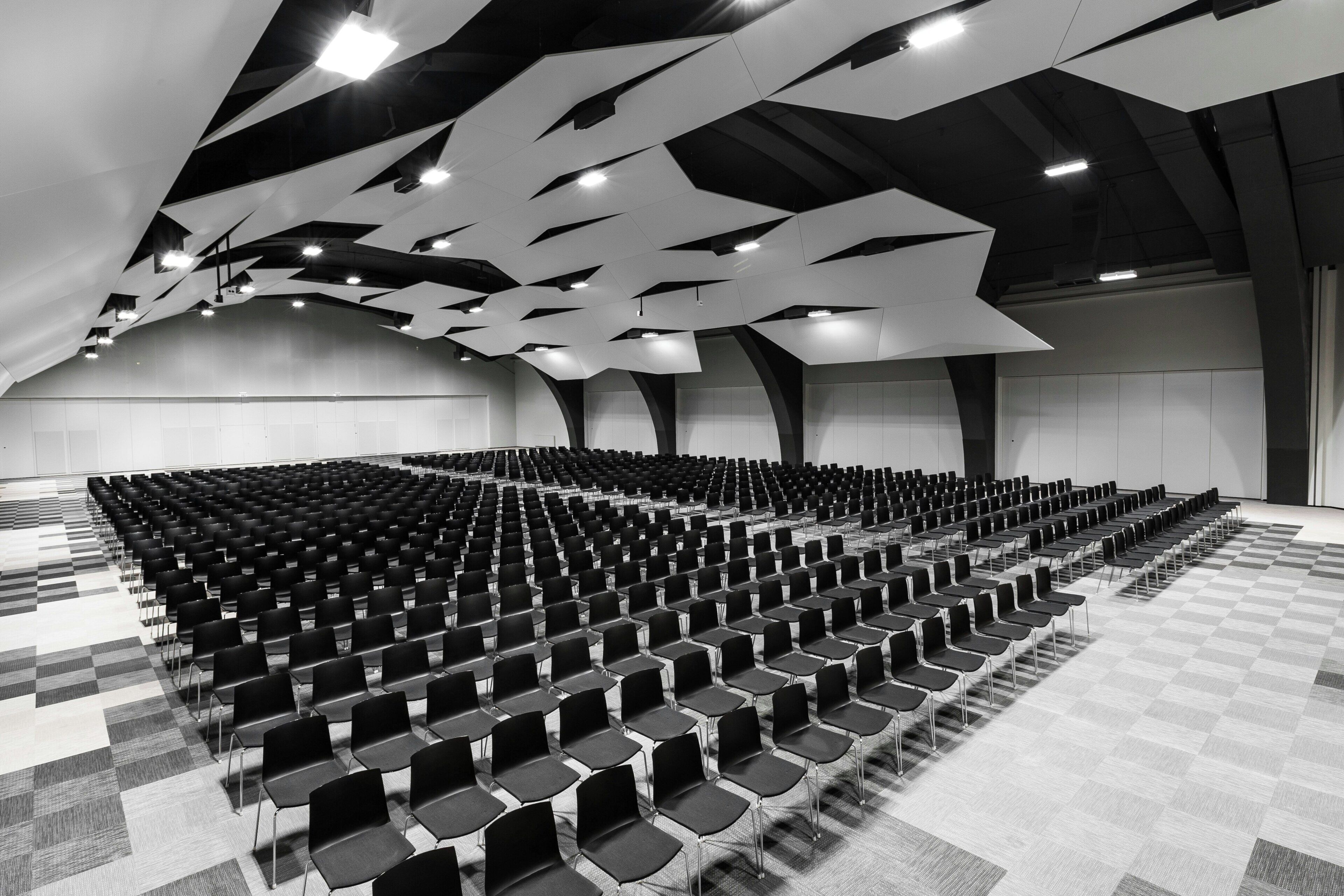 A large hall with rows of chairs and a geometric ceiling design.