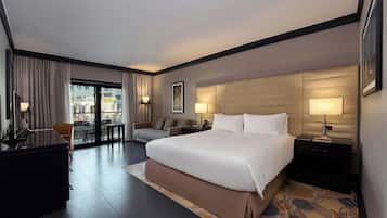 A hotel room with a large bed, a desk, a chair, a sofa, and a view of the city through the window.