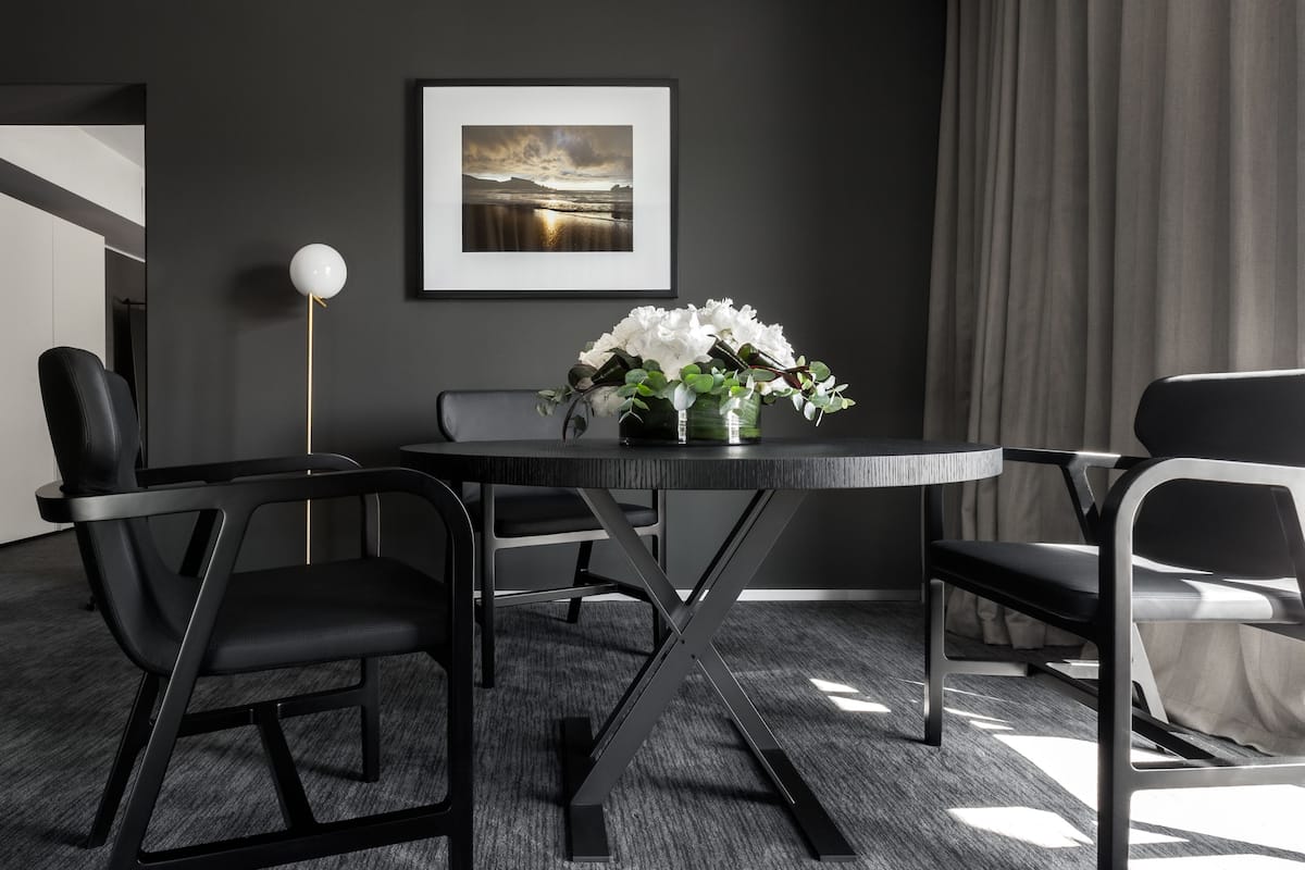 A modern conference room with a round table, black chairs, a vase with white flowers, and a framed picture on the wall.