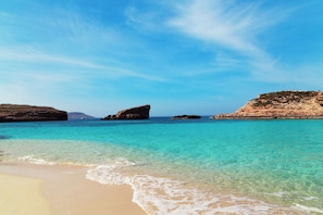 A beach with clear turquoise water, sandy shore, and rocky formations.