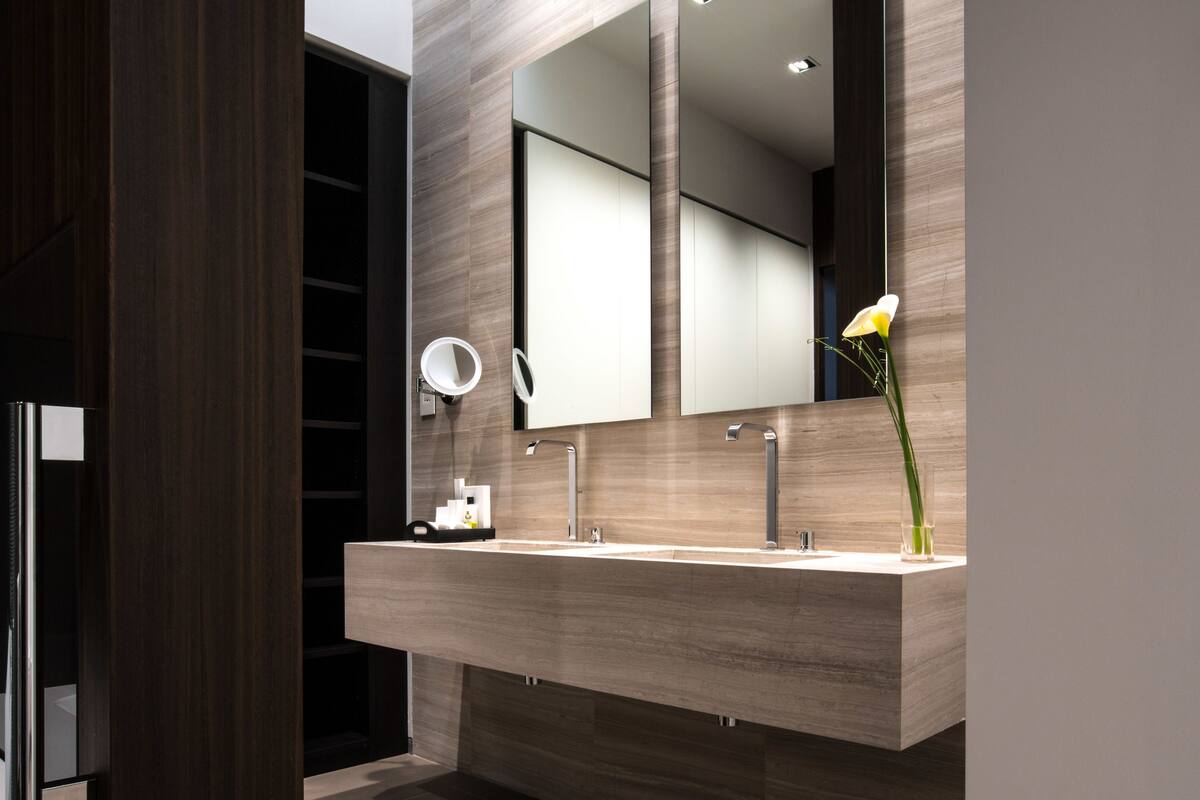 A modern bathroom with a large mirror, two sinks, and a vase with a single flower.