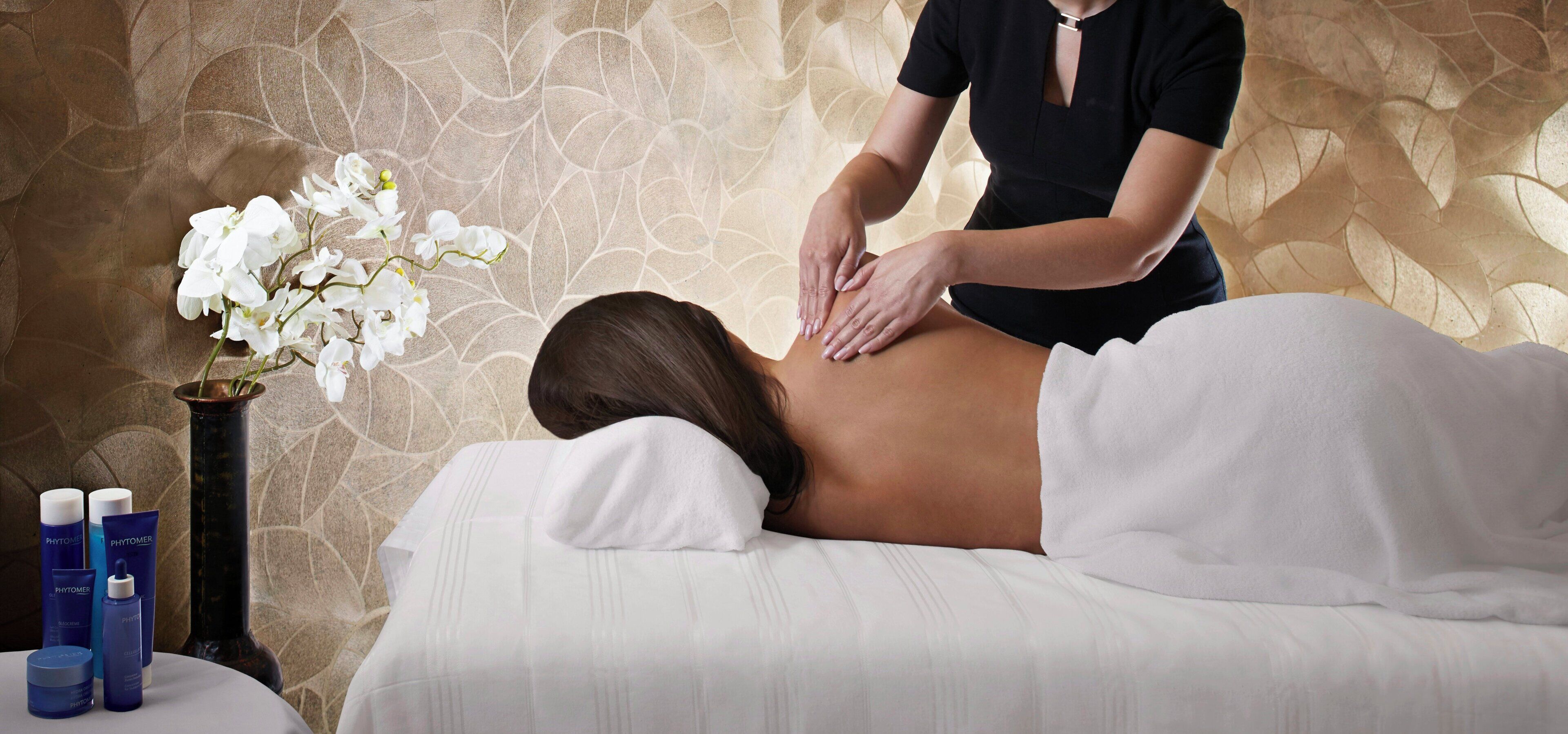 En massagebehandling i ett rum med en vägg som har ett mönster och en vas med vita blommor.
