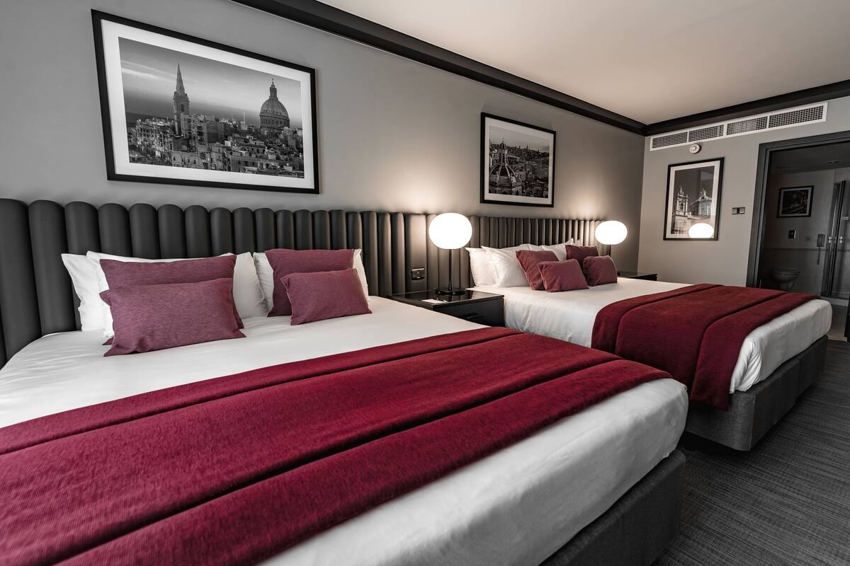 Quarto de hotel com duas camas, vista para a cidade e uma fotografia emoldurada na parede.