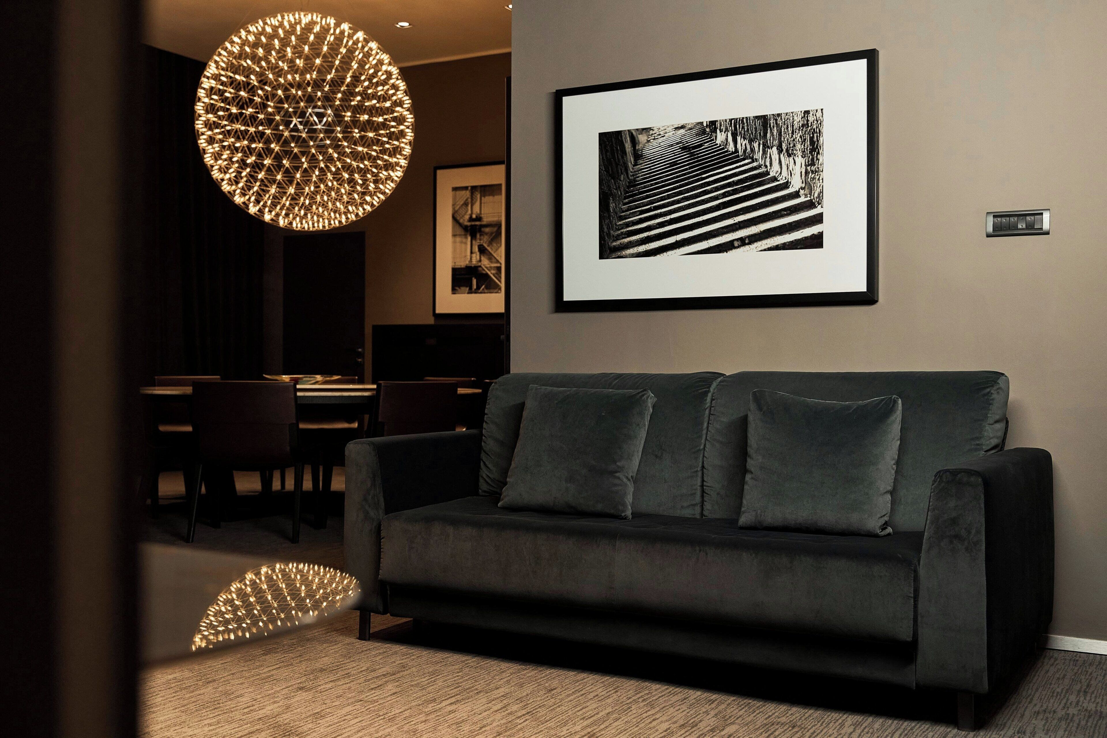 A modern living room with a dark sofa, a framed black and white photograph, and a unique spherical light fixture.