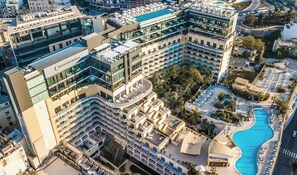 Un hotel de varios pisos con piscina en la azotea, asientos al aire libre y un patio ajardinado.