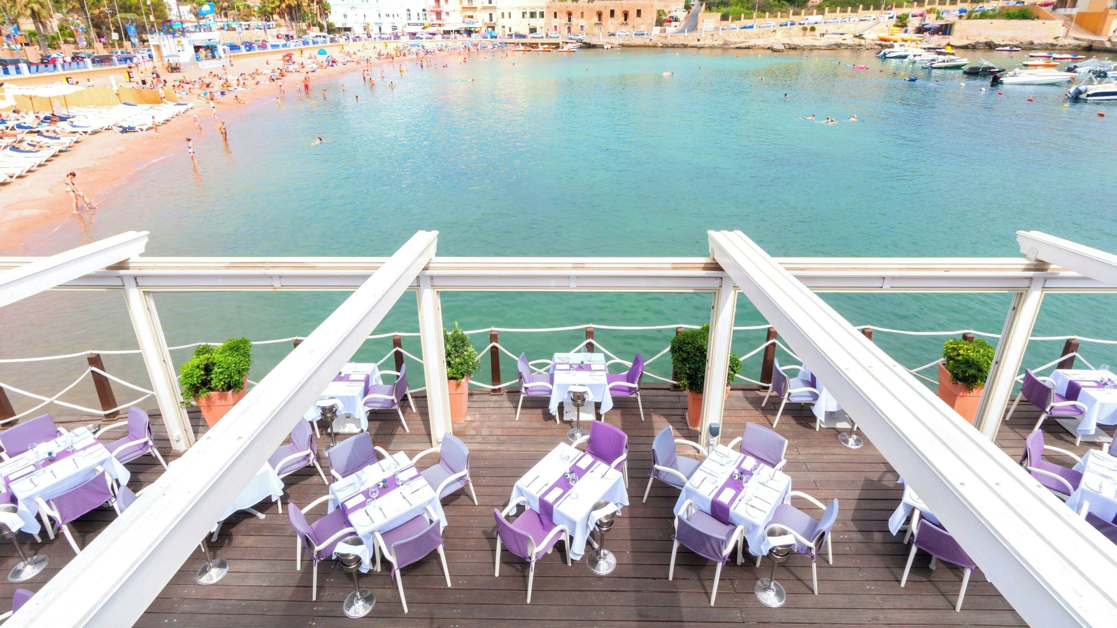 A deck with tables and chairs, overlooking a beach and water.