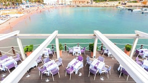 A deck with tables and chairs, overlooking a beach and water. - InterContinental Malta by IHG (St. Julian's)