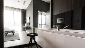 Habitación de hotel moderna con un espejo grande, un tocador blanco, un taburete pequeño y vistas al balcón.