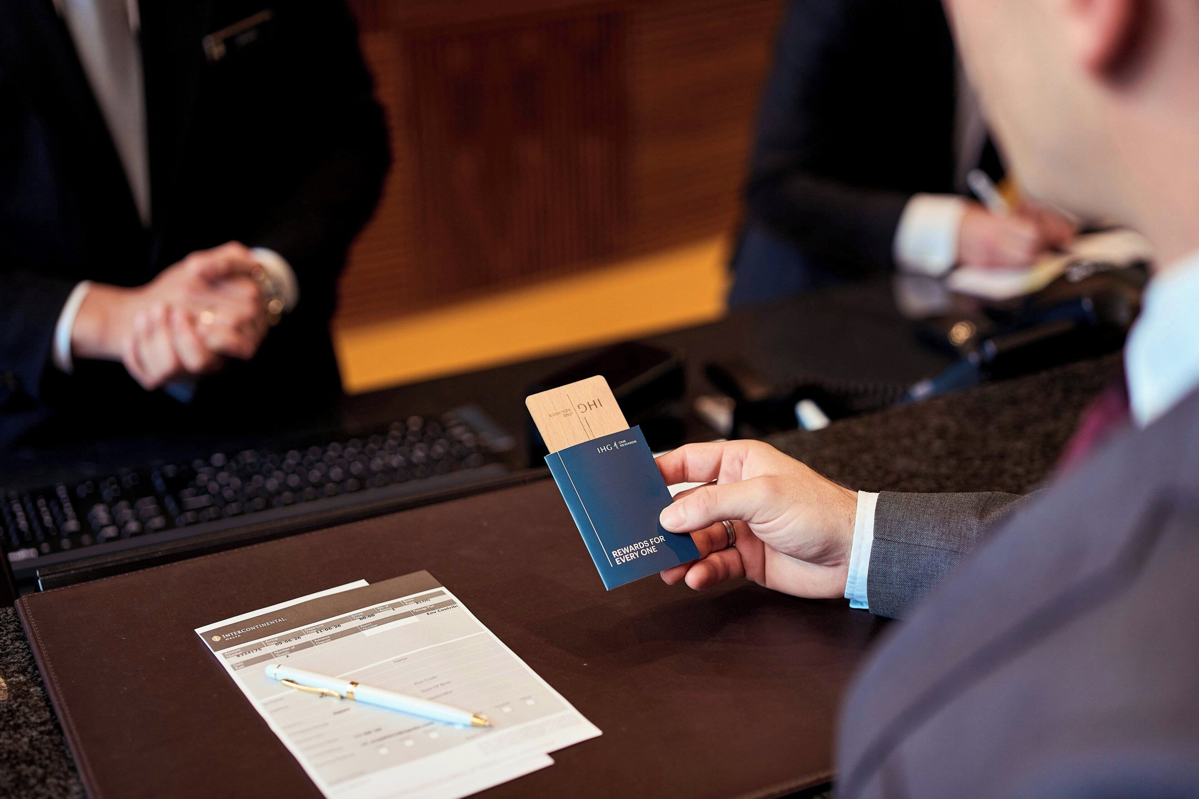 A person holding a blue card with text, seated at a desk with a laptop and documents.