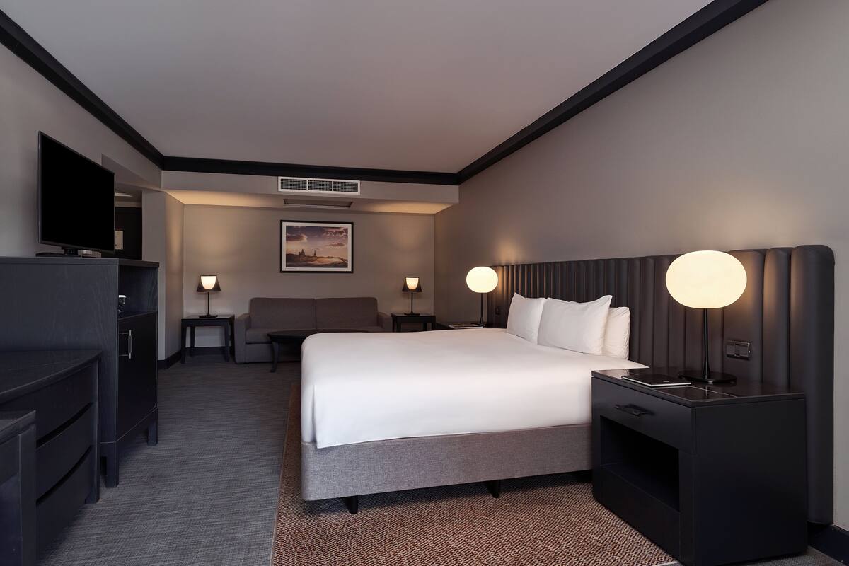 A modern hotel room with a large bed, a flat-screen TV, a desk, and a chair.