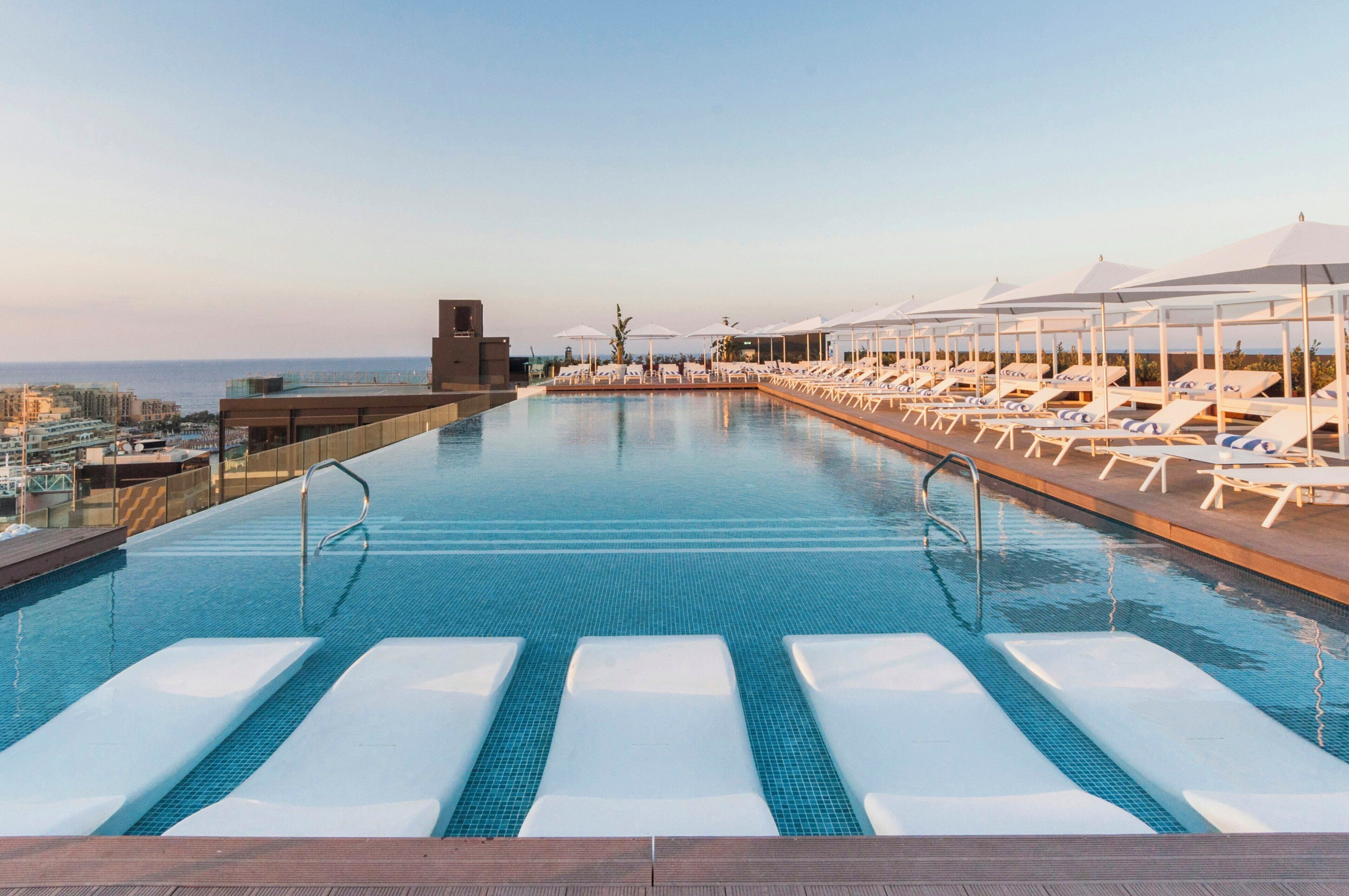 Una piscina con sillas de descanso y sombrillas, cielo despejado y vista al mar.