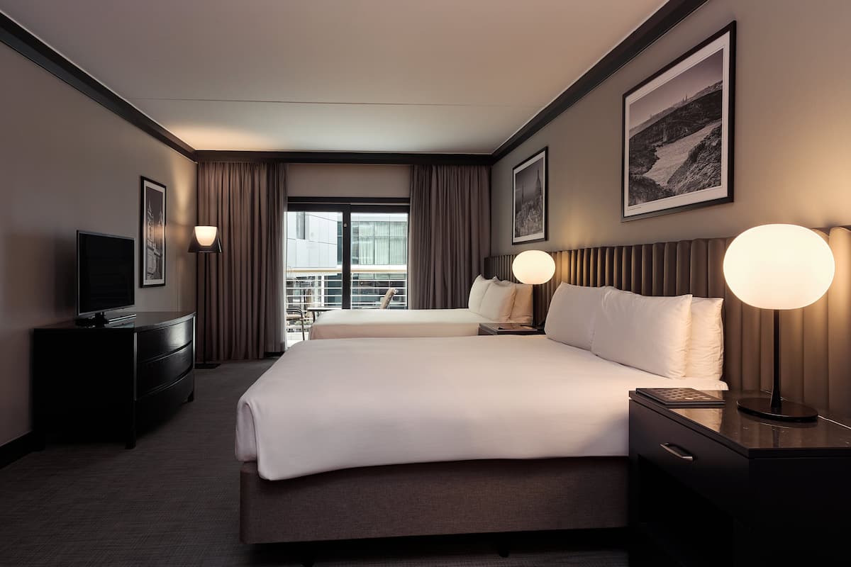 A hotel room with a large bed, a TV, a desk with a lamp, and a view of the cityscape.