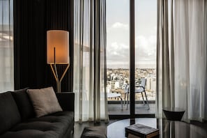 A modern living room with a sofa, a floor lamp, and a view of a cityscape through large windows.
