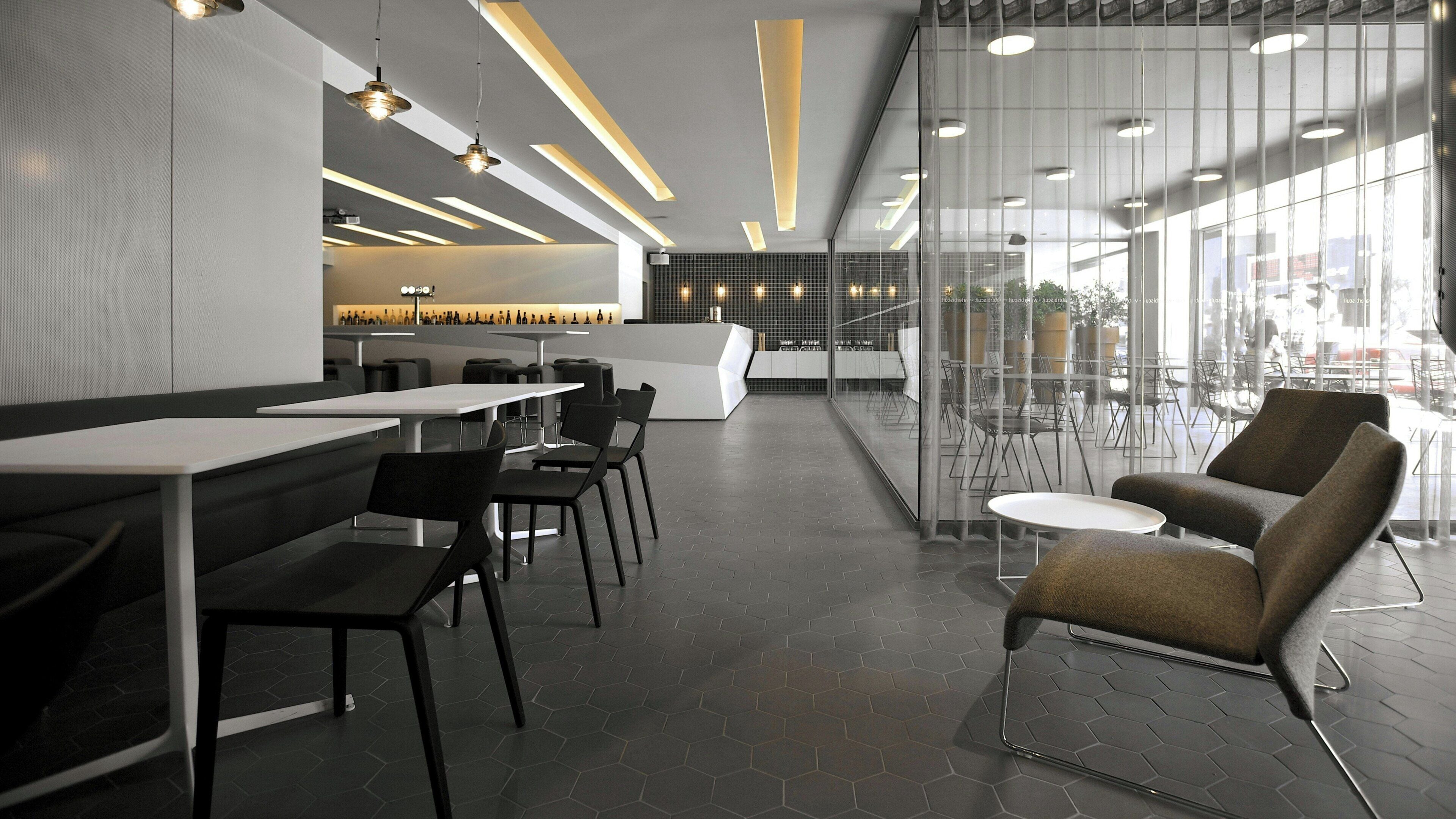 A modern interior with hexagonal floor tiles, black and white furniture, and a glass partition separating the dining area from the kitchen.