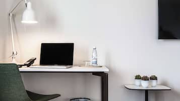 Ett skrivbord med en bärbar dator, en lampa, en vattenflaska och tre krukväxter.