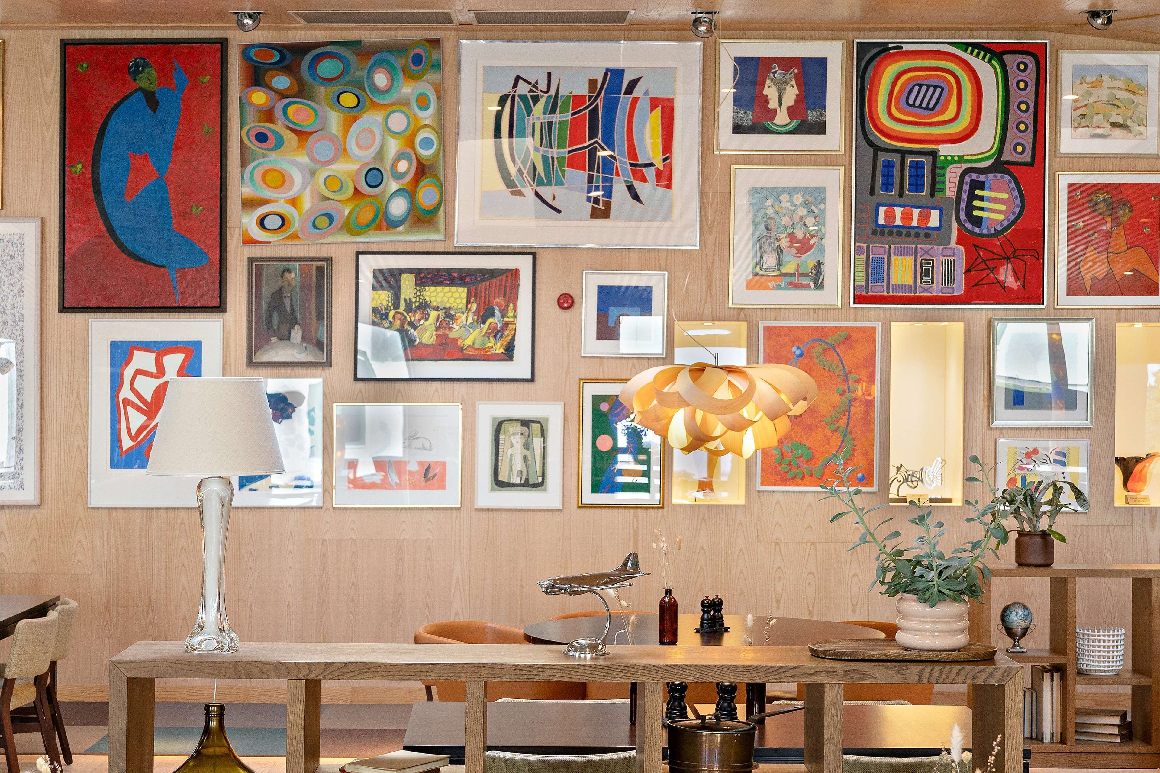 Una habitación con una mesa de madera, sillas y varias obras de arte enmarcadas en la pared.