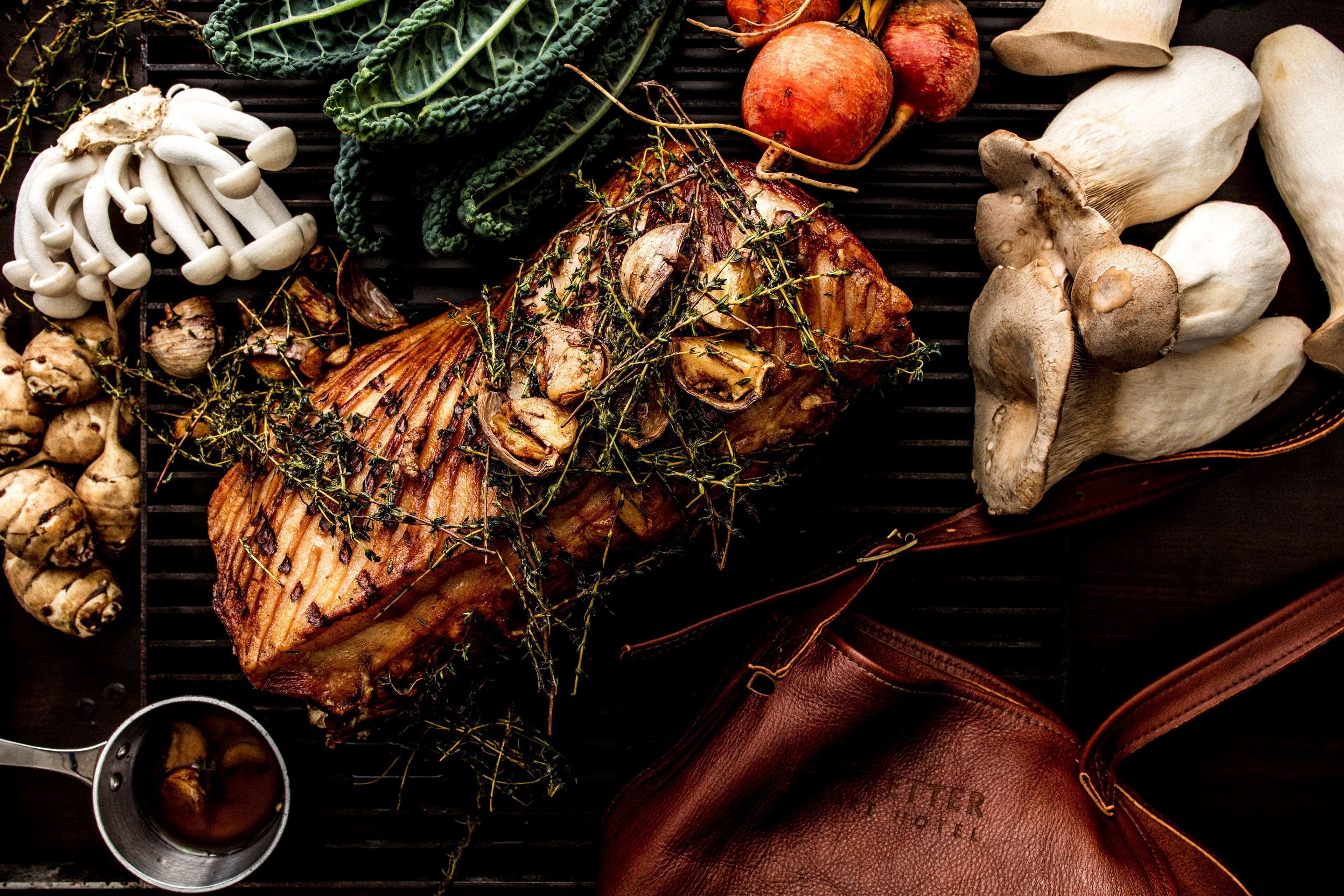 A roasted pork leg with herbs, mushrooms, and vegetables on a grill.