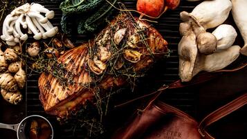 A roasted pork leg with herbs, mushrooms, and vegetables on a grill.