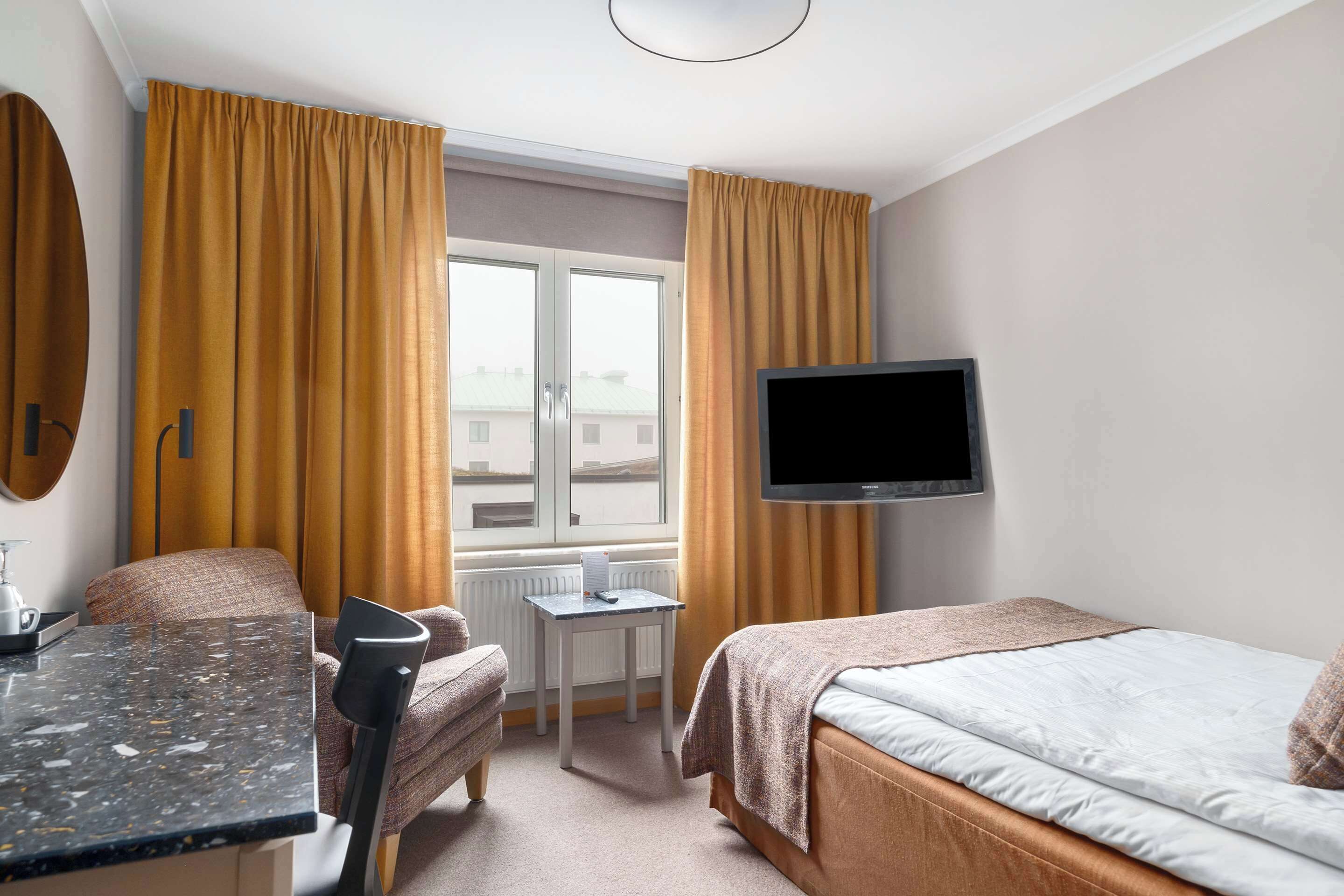 A hotel room with a bed, a desk, a chair, a television, and a window with curtains.