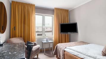 A hotel room with a bed, a desk, a chair, a television, and a window with curtains.