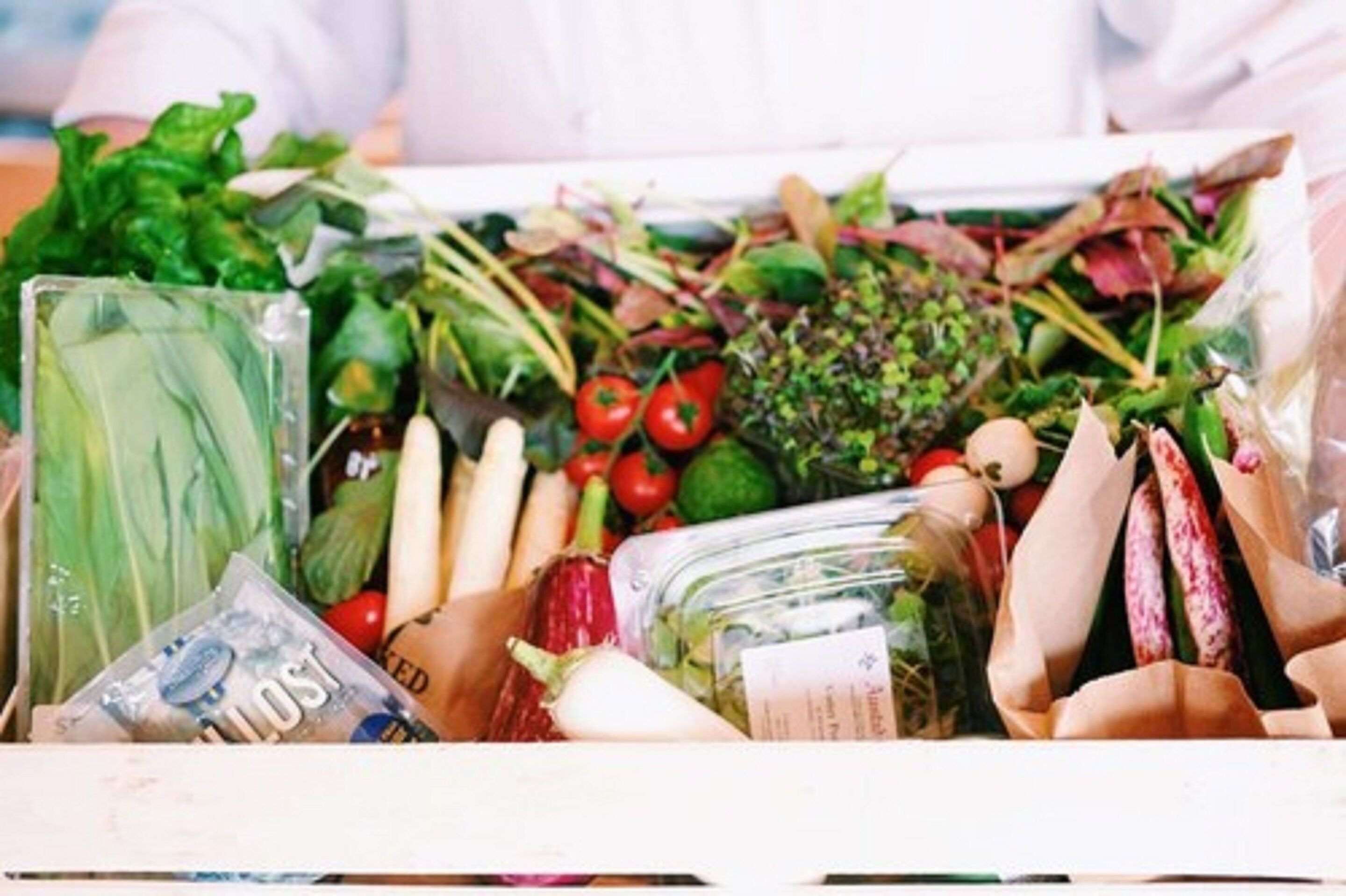 Una variedad de verduras frescas y hierbas en una caja, incluyendo hojas verdes, tomates y otros productos.