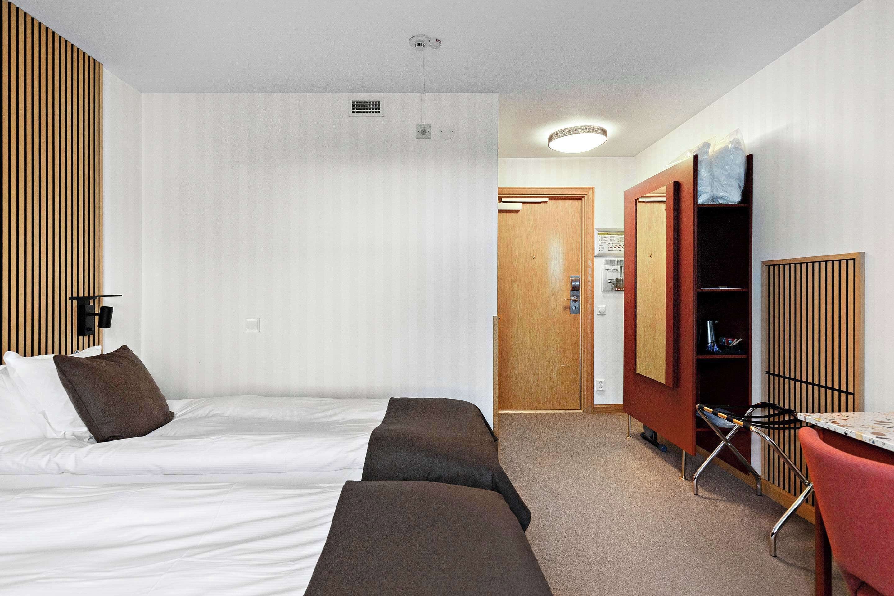 Ett hotellrum med en säng, ett skrivbord, en stol och en garderob.