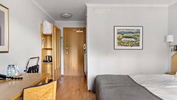 Habitación de hotel con cama, escritorio, silla, armario de madera y un cuadro en la pared.