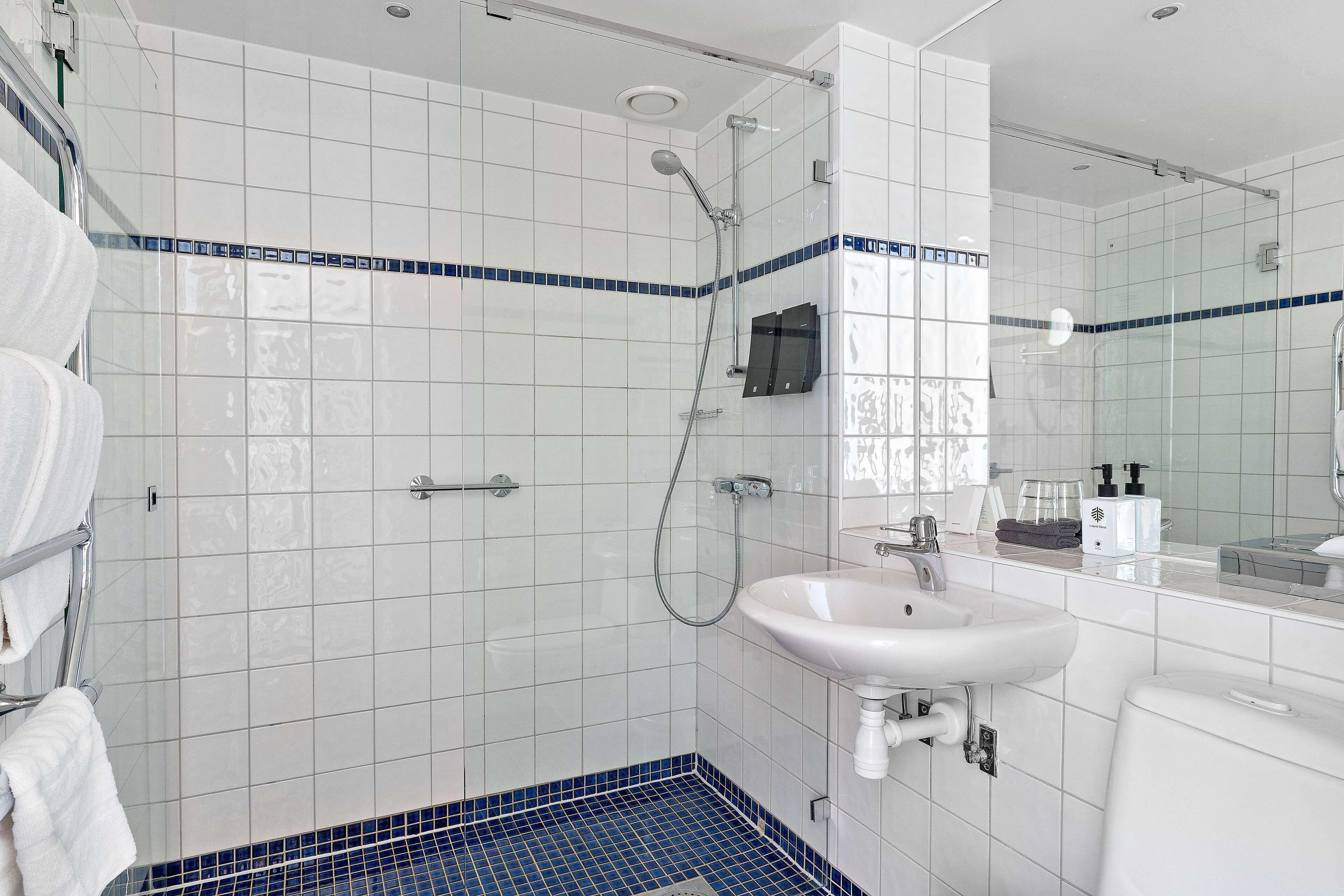 A modern bathroom with a glass shower enclosure, a white sink, and a tiled floor.
