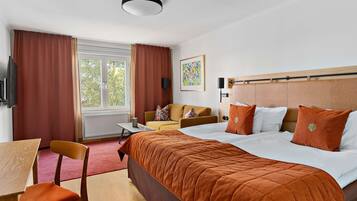 A hotel room with a bed, a desk, a chair, a sofa, and a window with curtains.