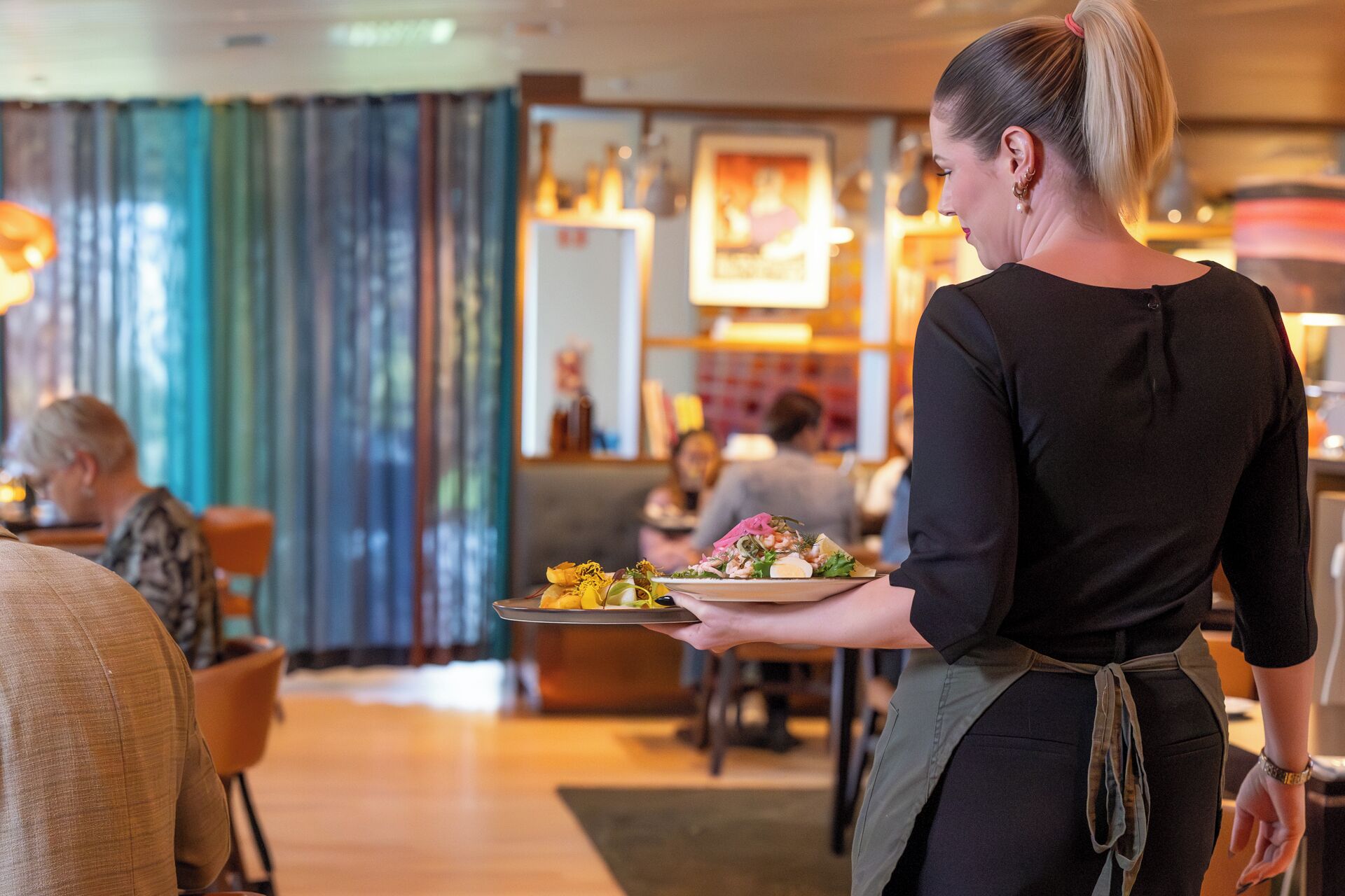 A person holding a plate with food, in a room with a counter and people in the background.