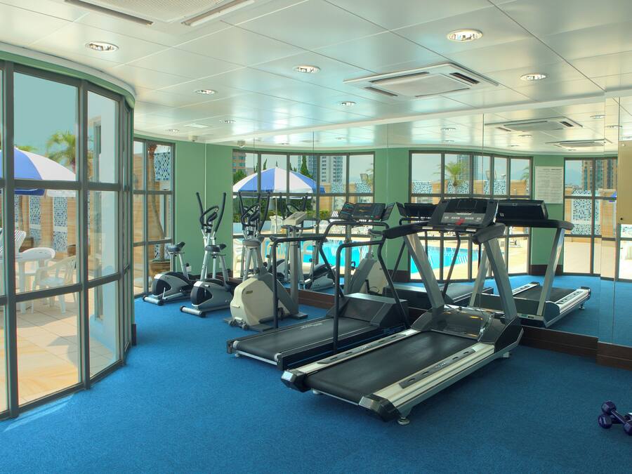 A gym with treadmills, exercise bikes, and a pool area with umbrellas.
