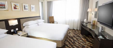 Una habitación de hotel con dos camas, un escritorio, un televisor y un ventanal con cortinas.