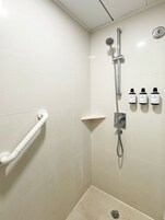 Zona de ducha con cabezal de ducha manual, grifo empotrado en la pared y tres botellas de champú.