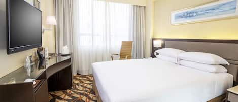 A hotel room with a large bed, a desk, a television, and a painting on the wall.