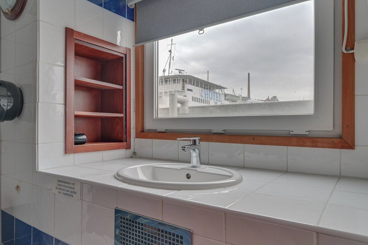 A bathroom with a large window, a sink, and a wooden shelf.