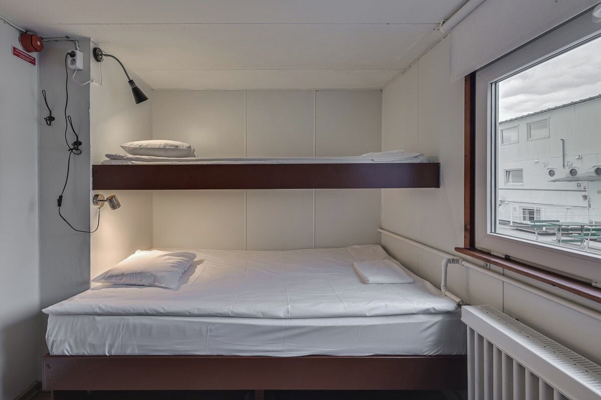A bunk bed with a window, white bedding, and a radiator.