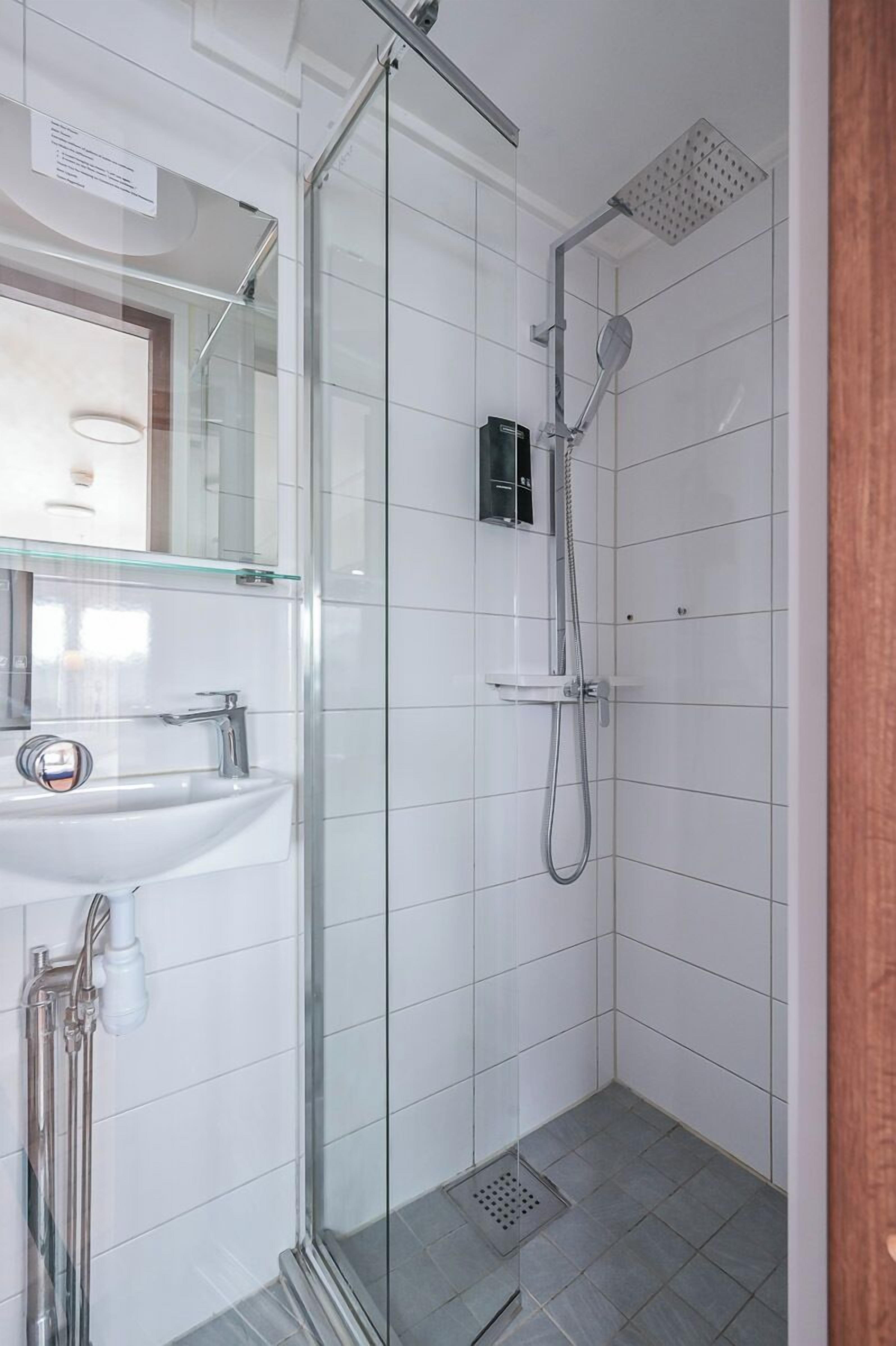 Un baño moderno con ducha de vidrio, lavamanos blanco y un espejo.