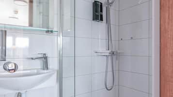 Un baño moderno con ducha de vidrio, lavamanos blanco y un espejo.