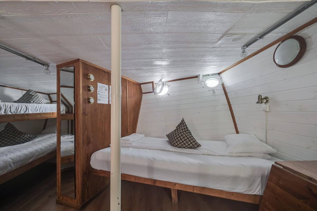 A dormitory room with bunk beds, a wooden wardrobe, a mirror, and a ceiling light fixture.